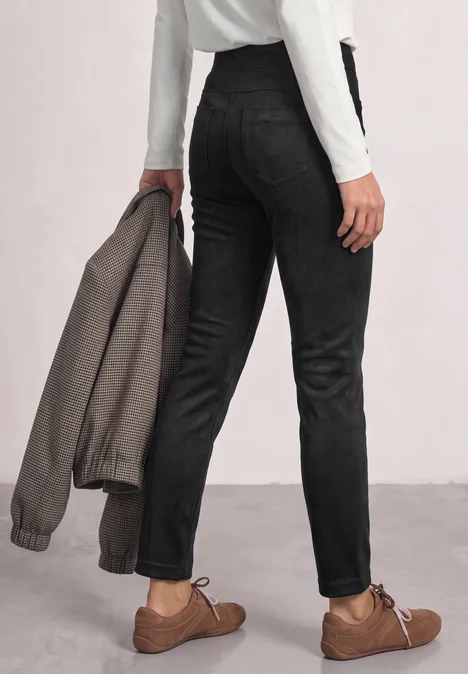 Personne de dos, pantalon noir, chaussures marron et une veste grise tenue à la main.