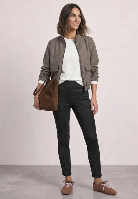 Femme en bomber kaki, top blanc, pantalon noir et sac brun assorti à ses chaussures.