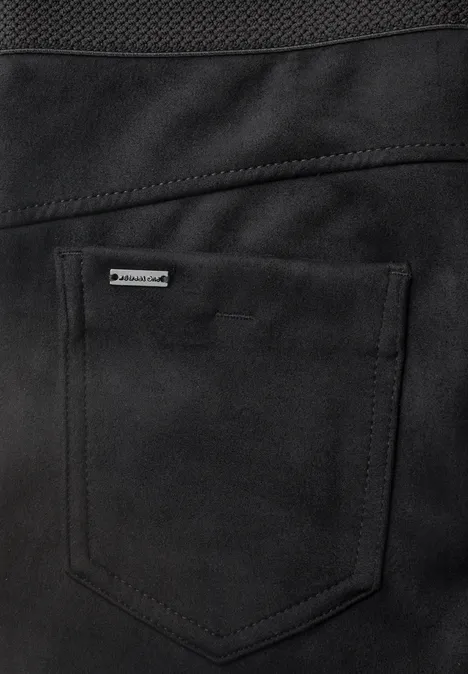 Gros plan sur une poche noire avec surpiqûres apparentes et petit logo métallique sur un vêtement.