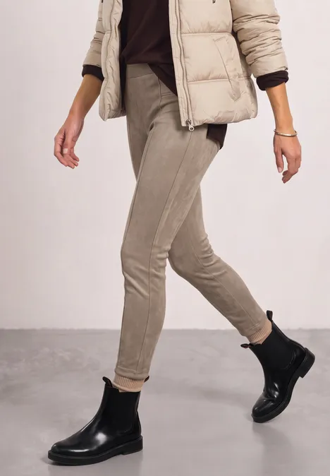 Persoon loopt in beige slim-fit broek, donsjas en zwarte Chelsea-laarzen.