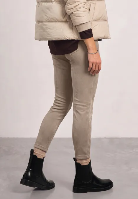 Persoon draagt een beige skinny broek, zwarte enkellaarsjes en een gewatteerd jack.