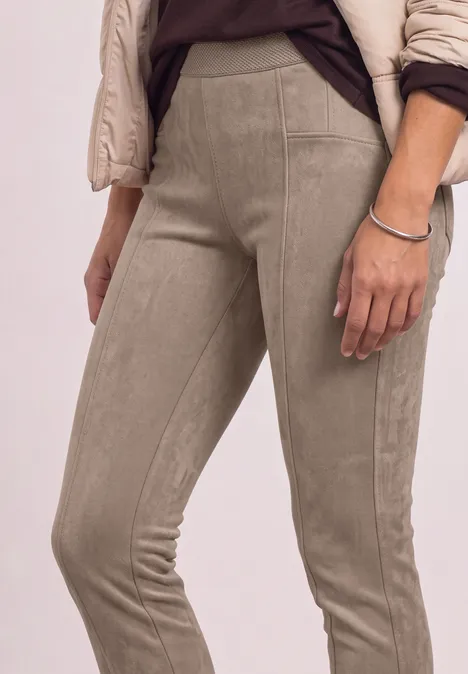Close-up van iemand in beige suède legging en een lichte gewatteerde jas