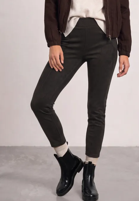 Pantalon slim olive, chaussettes blanches et bottines en cuir noir, porté avec un blouson marron et un tee-shirt blanc.