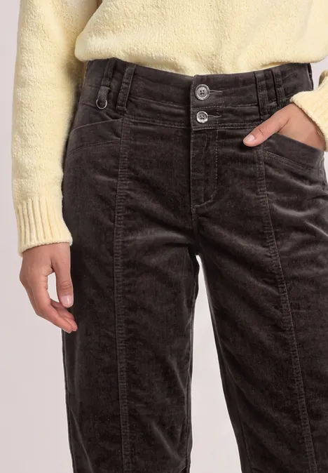 Eine Person trägt hellgelben Pullover und dunkelbraune Cordhose mit zwei Frontknöpfen.