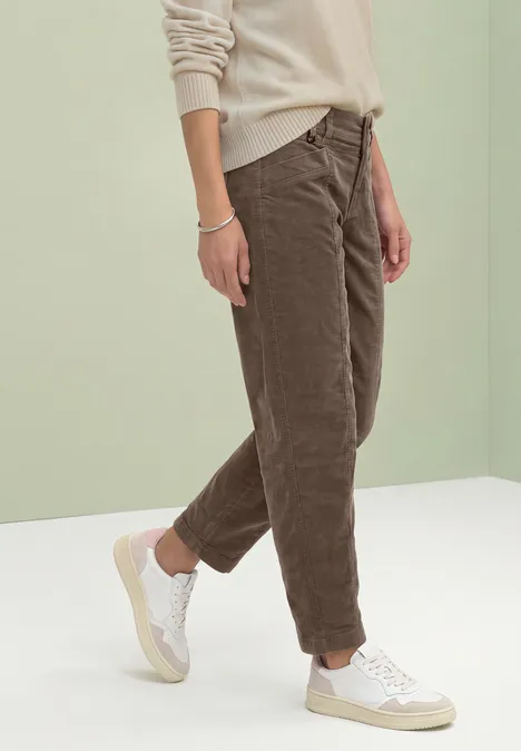 Barrel Leg Hose aus Cord im Casual Fit velvet mocha Person im beigen Pullover, brauner Cordhose und weißen Sneakern vor hellem Hintergrund.