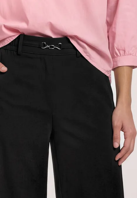 Schwarze weite Hose mit Gürtel und rosa Bluse, nur Oberkörper ab Taille zu sehen.