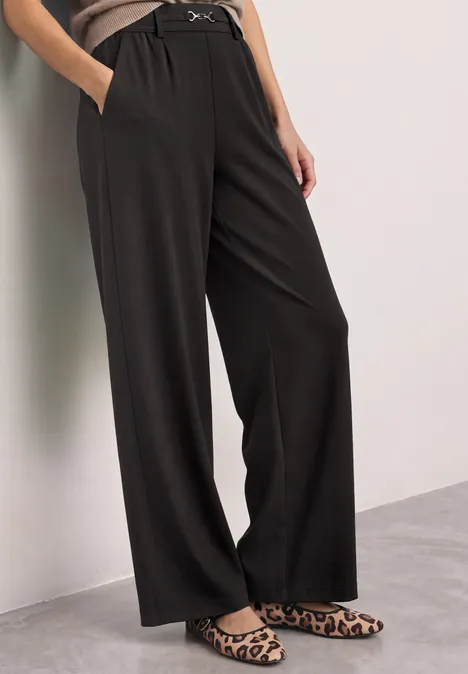 Schwarze, weite, hoch taillierte Hose mit Gürtelschlaufen, seitlichen Taschen, kombiniert mit Leo-Slippern.