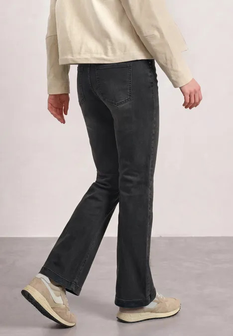High Waist Bootcut Jeans im Slim Fit Black Washed Person in schwarzen Jeans und beigen Sneakern vor neutralem hellen Hintergrund, grauer Boden.