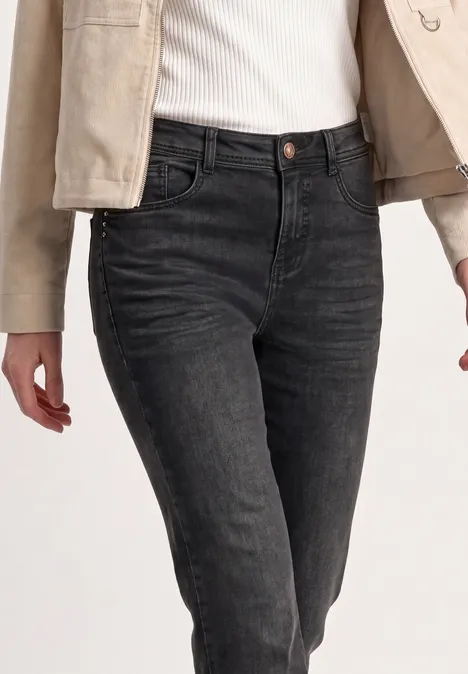 High Waist Bootcut Jeans im Slim Fit Black Washed Dunkle, eng geschnittene Damenjeans mit hohem Bund, kombiniert mit weißem Top und hellbeiger Jacke.