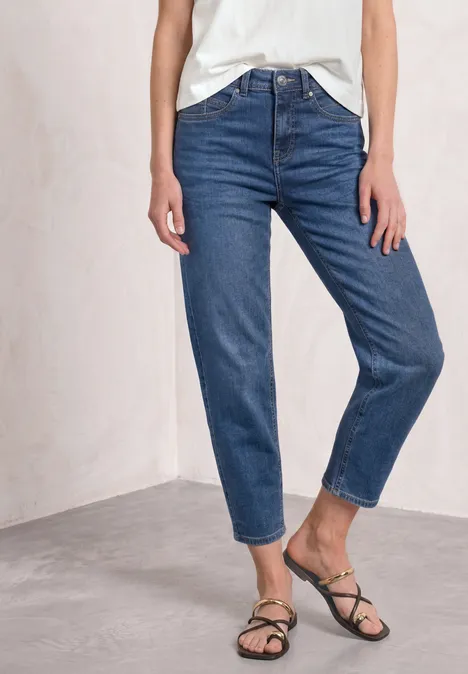 High Waist Barrel Leg Jeans im Loose Fit Medium Blue washed Frau trägt blaue Jeans und schwarze Sandalen, stehend vor hellem Hintergrund.