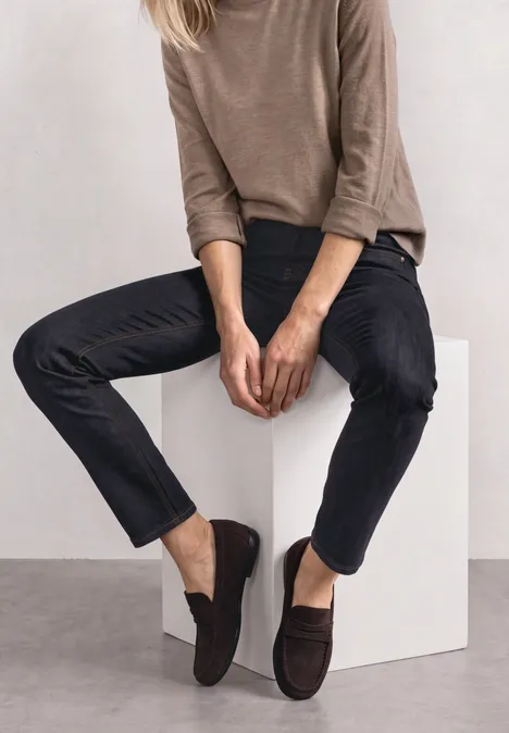 Jean taille moyenne, coupe Slim Leg, style décontracté Deep Rinse Washed Person sitzt auf einem weißen Würfel, trägt hellbraunen Pullover, dunkle Jeans und braune Loafers.