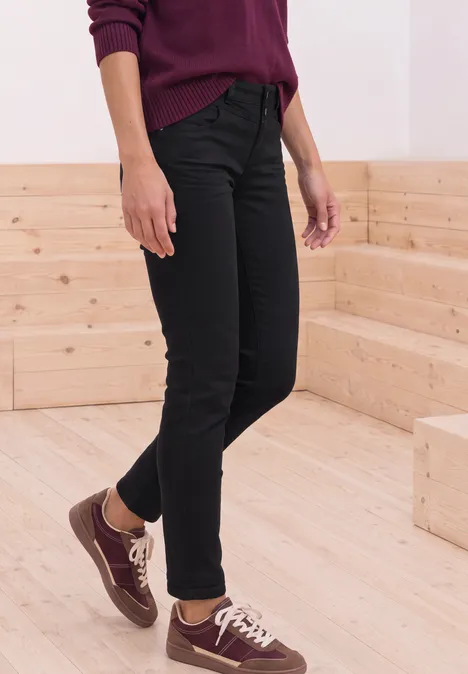 Mid Waist Slim Leg Jeans im Casual Fit Black Clean Washed Person in schwarzer Jeans und weinrotem Pullover mit braunen Sneakern auf Holztreppe