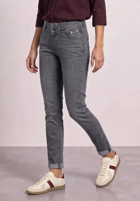 Grijze jeans met witte sneakers en een bordeauxrood shirt.