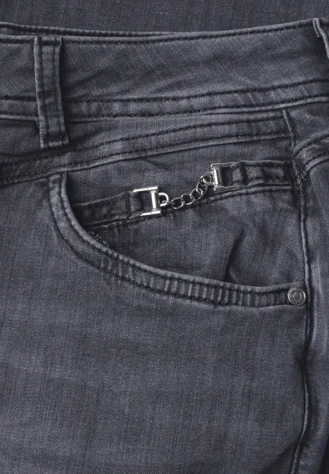 Donkere spijkerbroek met zichtbare stiksels en een klein zilveren kettinkje aan de voorzak.