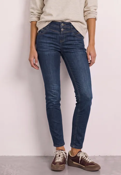 Mid Waist Slim Leg Jeans z ozdobnym detalem Dark Blue Soft Washed Osoba ma na sobie ciemnoniebieskie obcisłe jeansy z wysokim stanem i brązowe sneakersy.