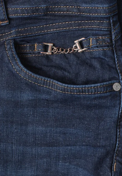 Mid Waist Slim Leg Jeans z ozdobnym detalem Dark Blue Soft Washed Zbliżenie niebieskich dżinsów z ozdobnym srebrnym łańcuszkiem przy przodzie kieszeni.