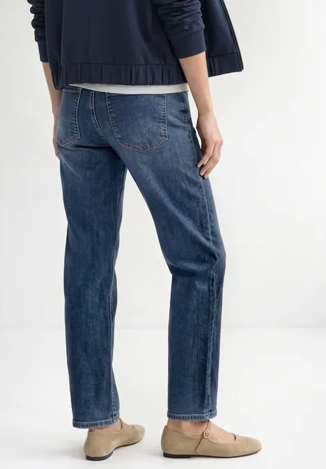 Straight Leg Jeans mit Gürtel Mid Blue Random Washed Rückansicht einer Person in blauen Jeans, dunklem Oberteil und beigen Halbschuhen.