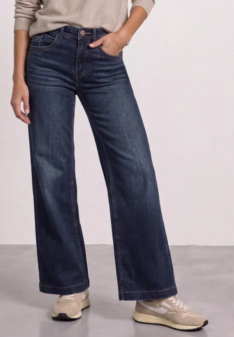 Person trägt weite dunkelblaue Jeans und helle Sneaker.