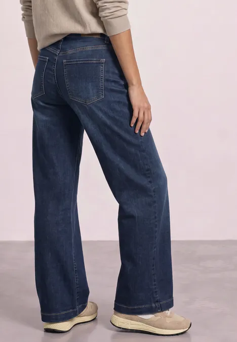 Rückansicht einer Person mit weitem, dunkelblauen Jeanshose und hellen Schuhen.