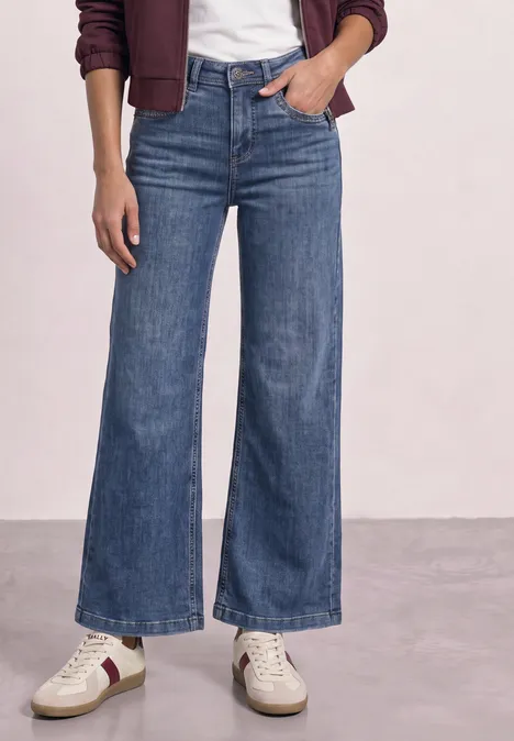 Frau trägt hoch taillierte, weit geschnittene Jeans, weiße Sneaker und eine burgunderrote Jacke.