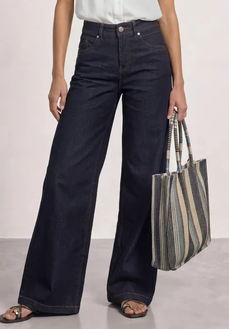 Jean large taille haute foncé, sandales ouvertes et sac en tissu rayé.