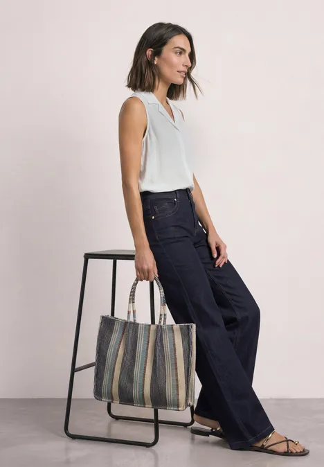 Femme en top blanc, pantalon large foncé et sac rayé.
