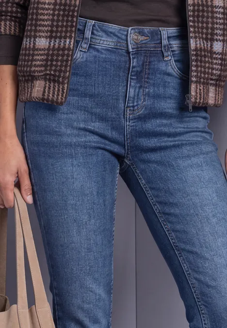 Gros plan d'une personne en jean taille haute bleu, gilet à carreaux, t-shirt noir et sac tote beige.