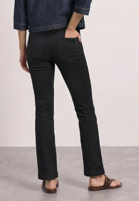 Une personne vue de dos porte un jean évasé noir, une veste en jean et des sandales.