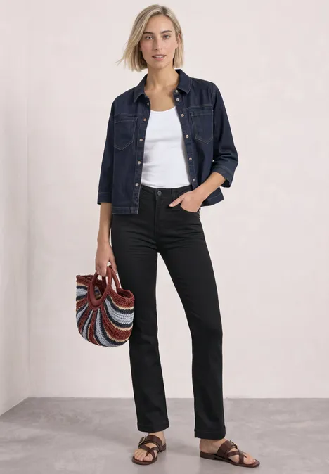 Femme en veste en jean, débardeur blanc et pantalon noir, sandales, sac coloré.