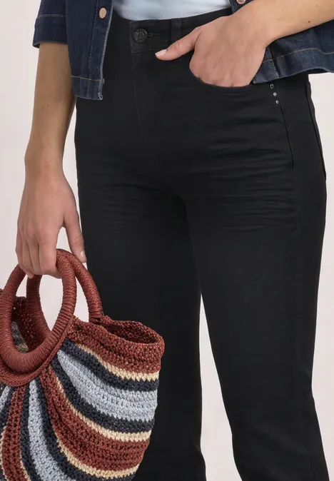 Person en pantalon noir tient un sac en tricot rayé multicolore au niveau de la hanche.