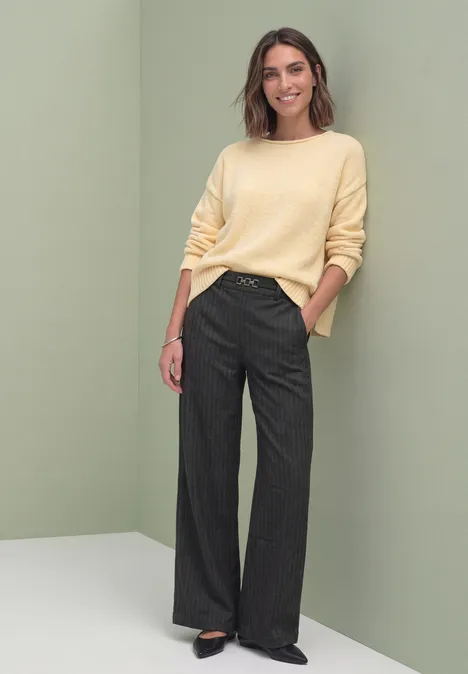 Stright Leg Hose mit Fishbone-Muster Black Eine Frau steht locker vor grünem Hintergrund, trägt gelben Pullover und weite graue Hose, lächelt.