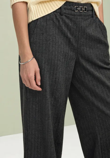 Stright Leg Hose mit Fishbone-Muster Black Person trägt hellen Strickpullover und weite, dunkelgraue Nadelstreifenhose mit Gürtel
