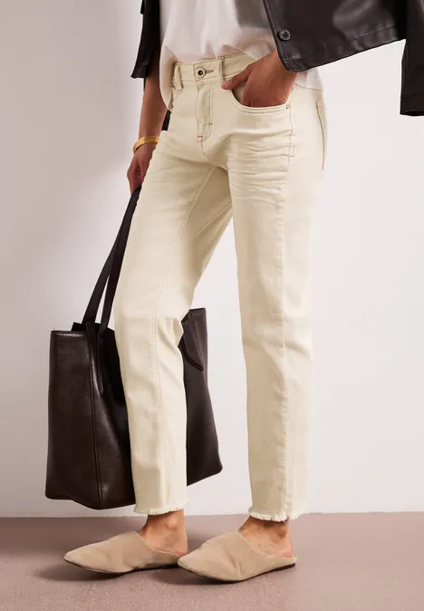 Frau in hellgelben Jeans mit ausgefranstem Saum, beigen Mules und großer dunkelbrauner Ledertasche.