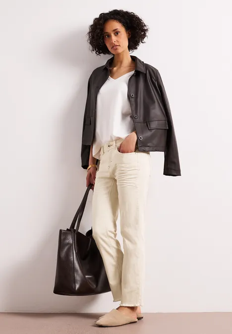 Person in schwarzer Lederjacke, weißem Top, beiger Hose und mit großer schwarzer Tasche.