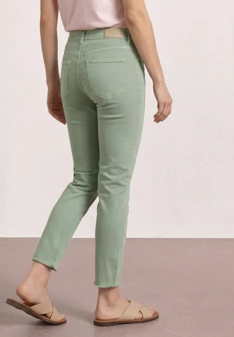 Vrouw van achteren in lichtgroene jeans en beige sandalen tegen een neutrale achtergrond.