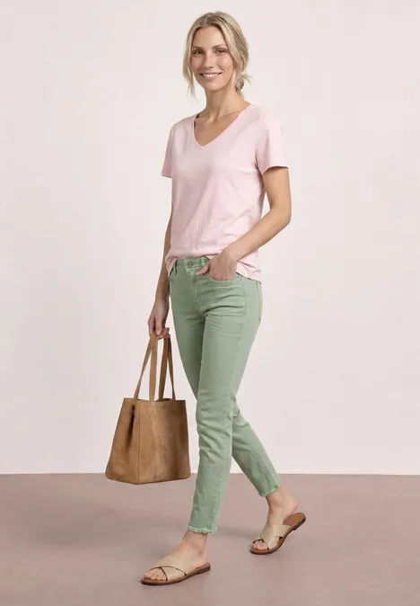 Vrouw in roze T-shirt, groene broek, sandalen en bruine tas.