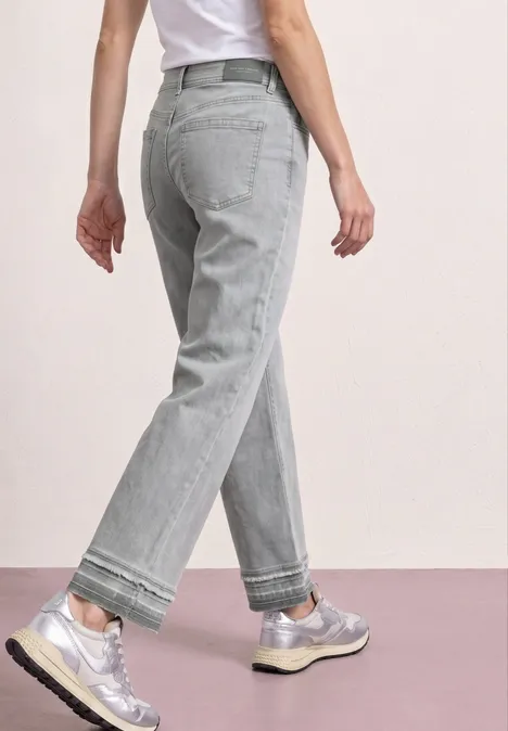 Person trägt graue, weite Jeans und silberne Sneaker, Blick von hinten, lässiger Stil.