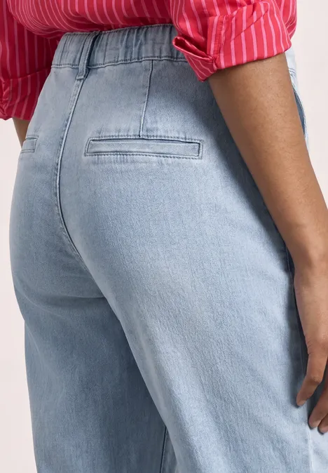 Eine Person von hinten in hellblauen Jeans und rotem Hemd.