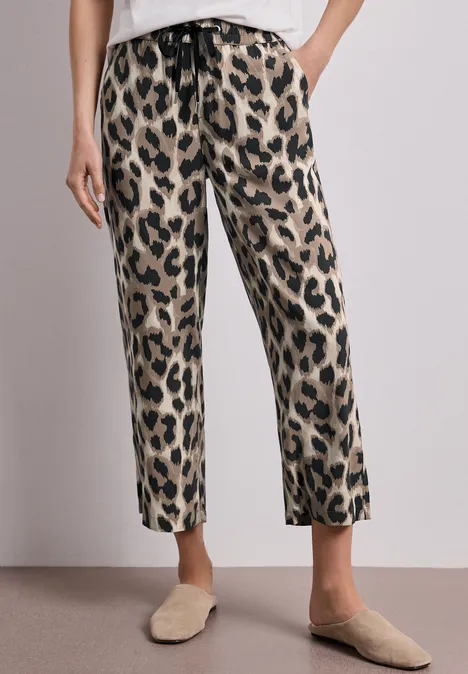 Beine in lässigen, gerade geschnittenen Leopardenmuster-Hosen mit Gürtelband, kombiniert mit beigen Slippern.