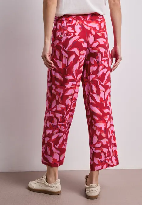 Eine Person von hinten trägt rote, locker sitzende Hose mit pink-rosa Blattmuster und weitem Schnitt.