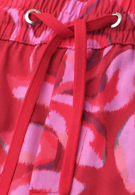 Roter Stoff mit pinkem Blumenmuster und roten Kordeln durch silberne Ösen.