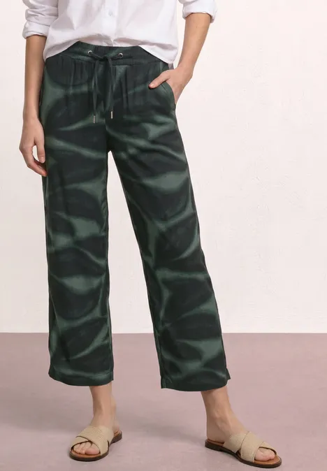 Frau trägt weite, dunkelgrüne, gemusterte Stoffhose mit Tunnelzug und flachen Sandalen.