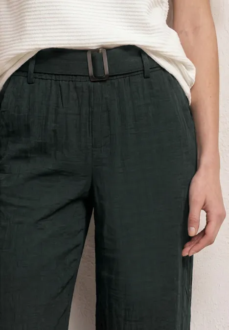 Eine Person trägt eine weiße gestreifte Bluse und schwarze Hose mit Gürtel, Bildausschnitt vom Oberkörper.