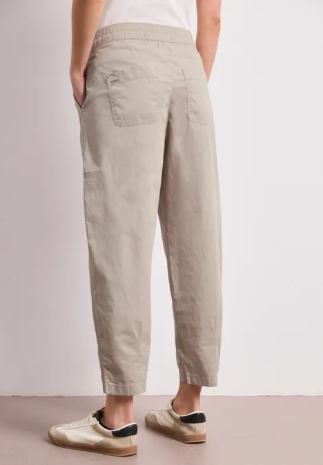 Rückansicht einer Person, die beige, locker sitzende Hose mit elastischem Bund und Knöchelabschlüssen trägt.