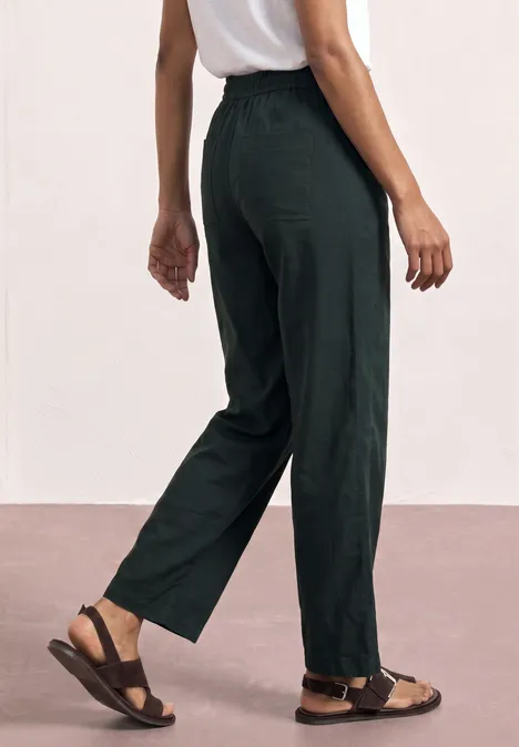 Eine Person trägt schwarze, locker sitzende Hose und braune Sandalen vor hellem Hintergrund.