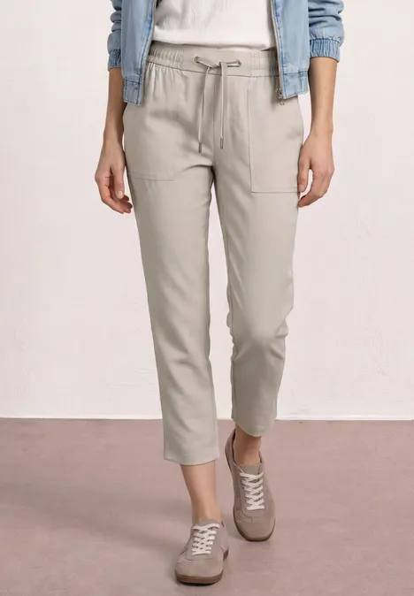 Pantalon clair chevillant en toile avec cordon et poches, associé à des baskets et une veste en jean.