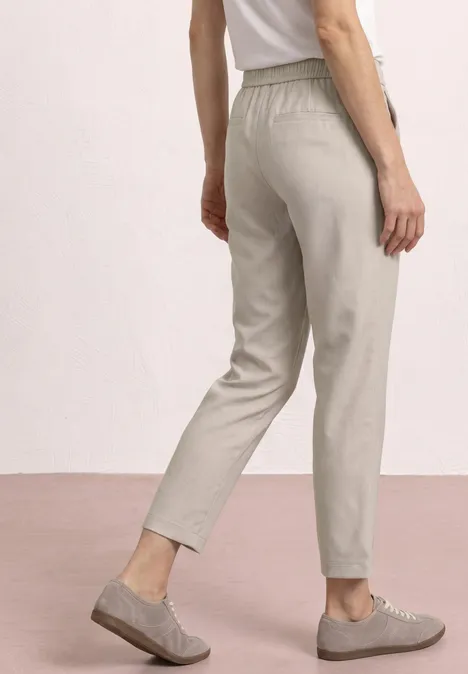 Pantalon gris à taille élastique, coupe slim et longueur cheville, porté avec des derbies grises.