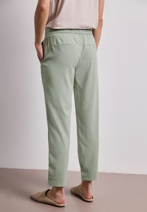 Person von hinten, trägt hellgrüne Jogginghose und Flip-Flops, Hände in den Taschen.