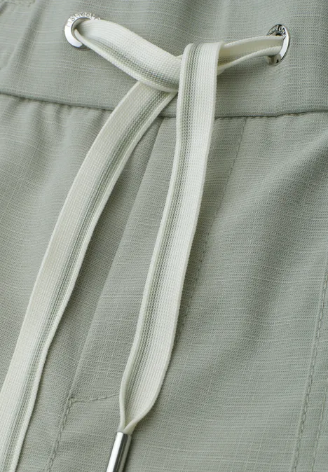 Detailaufnahme einer hellgrünen Hose mit weißem Kordelzug am Bund.