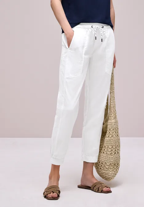 Weiße Leinenhose mit Tunnelzug & Taschen, kombiniert mit Sandalen und geflochtener Strohtasche.